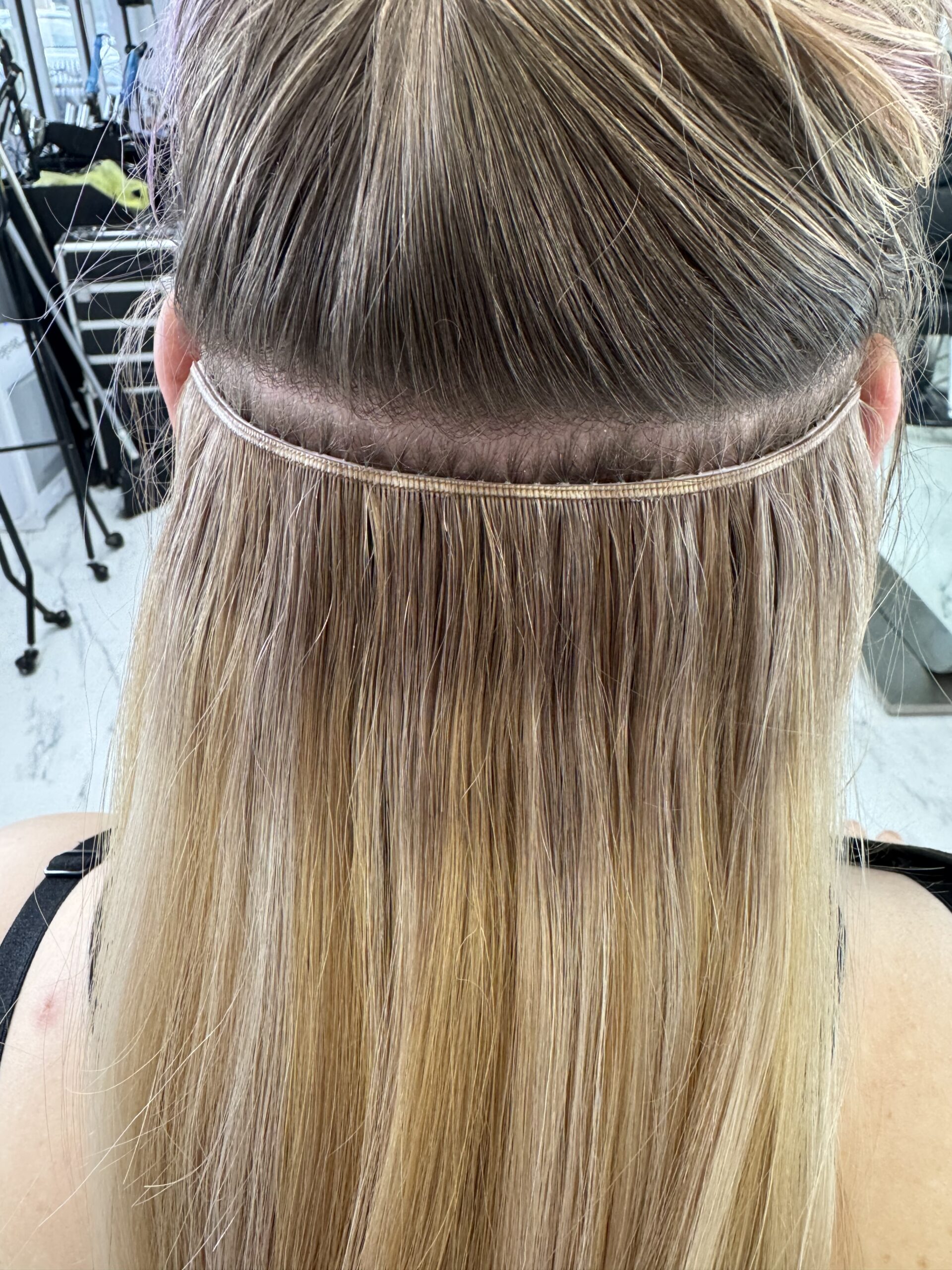 Hair extension application in progress, showcasing blended natural and extension hair. The setup highlights salon techniques for length enhancement.