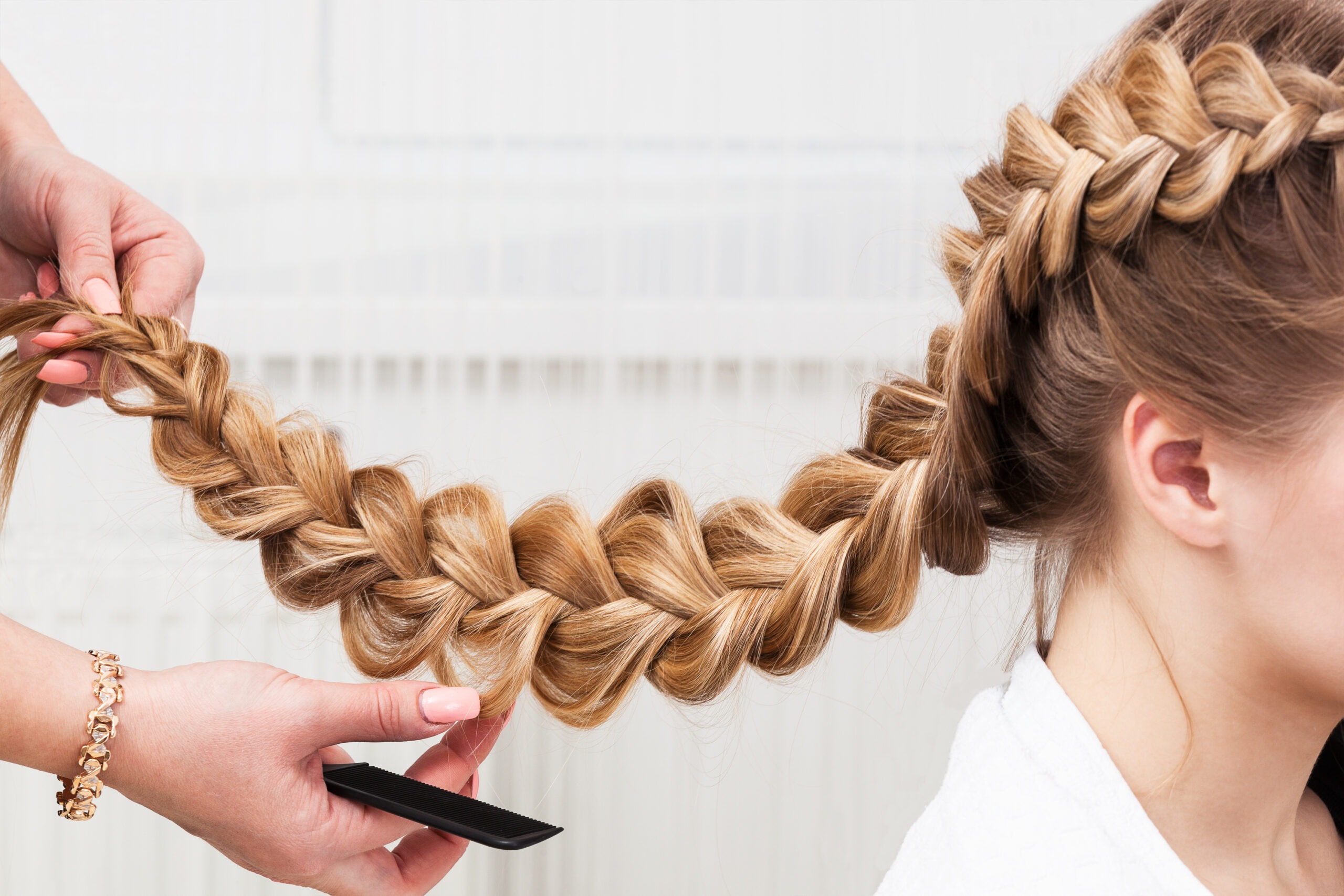 A stylist intricately braids long blonde hair, showcasing detailed, large sections of the braid and the process of hairstyling.