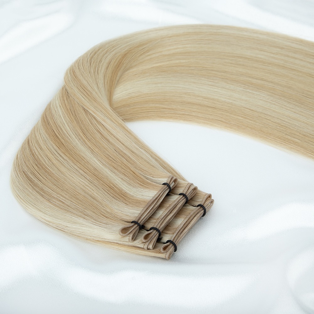 Long, straight blonde hair extensions are neatly arranged and tied with black elastics, displayed on a soft white fabric background.