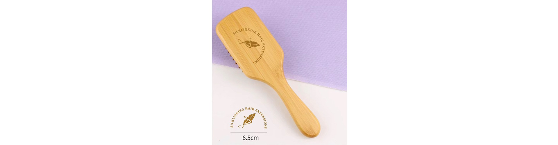 Bamboo hair extension brush labeled "Silklinking Hair Extensions," measuring 6.5 cm, set against a light purple background. Ideal for hair care.