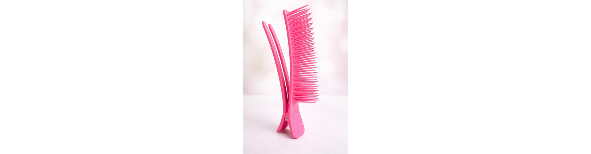 Bright pink comb with a unique design, showcasing long and short teeth, placed upright against a soft, blurred background. Ideal for hairstyling tips.
