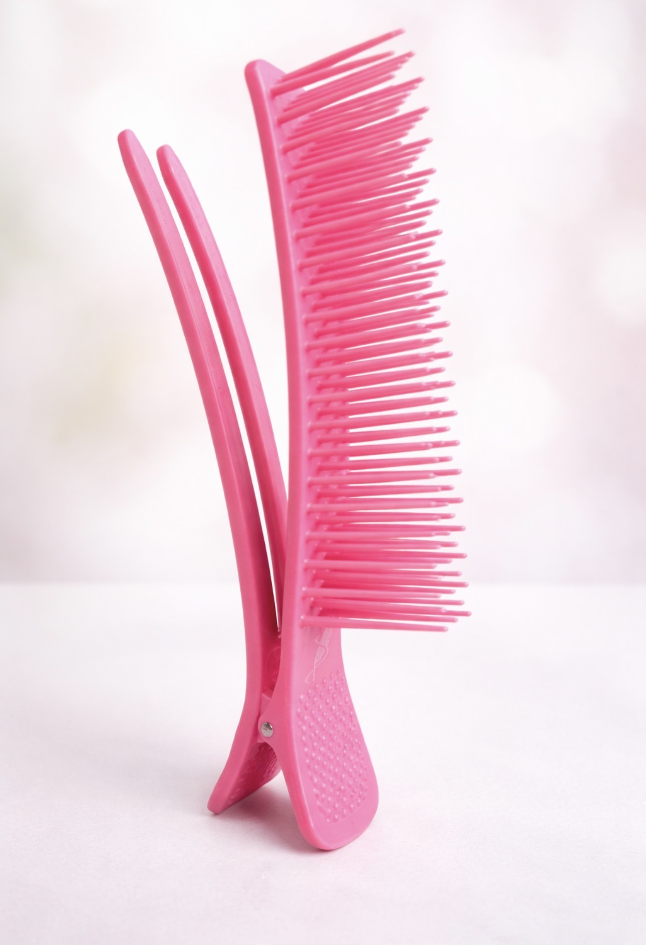 Bright pink comb with a unique design, showcasing long and short teeth, placed upright against a soft, blurred background. Ideal for hairstyling tips.